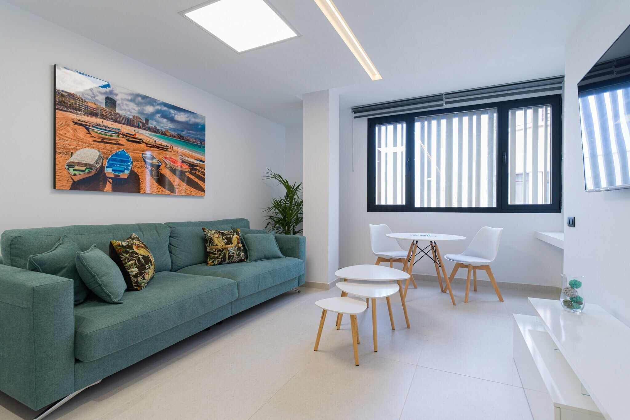 A modern living room with a teal sofa, a coffee table, and a dining area with chairs and a small table.