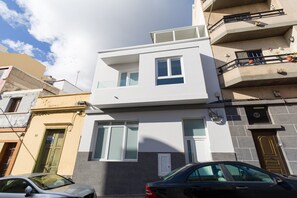 Ein modernes, zweistöckiges Gebäude mit Balkonen, ein Auto davor und ein klarer Himmel.