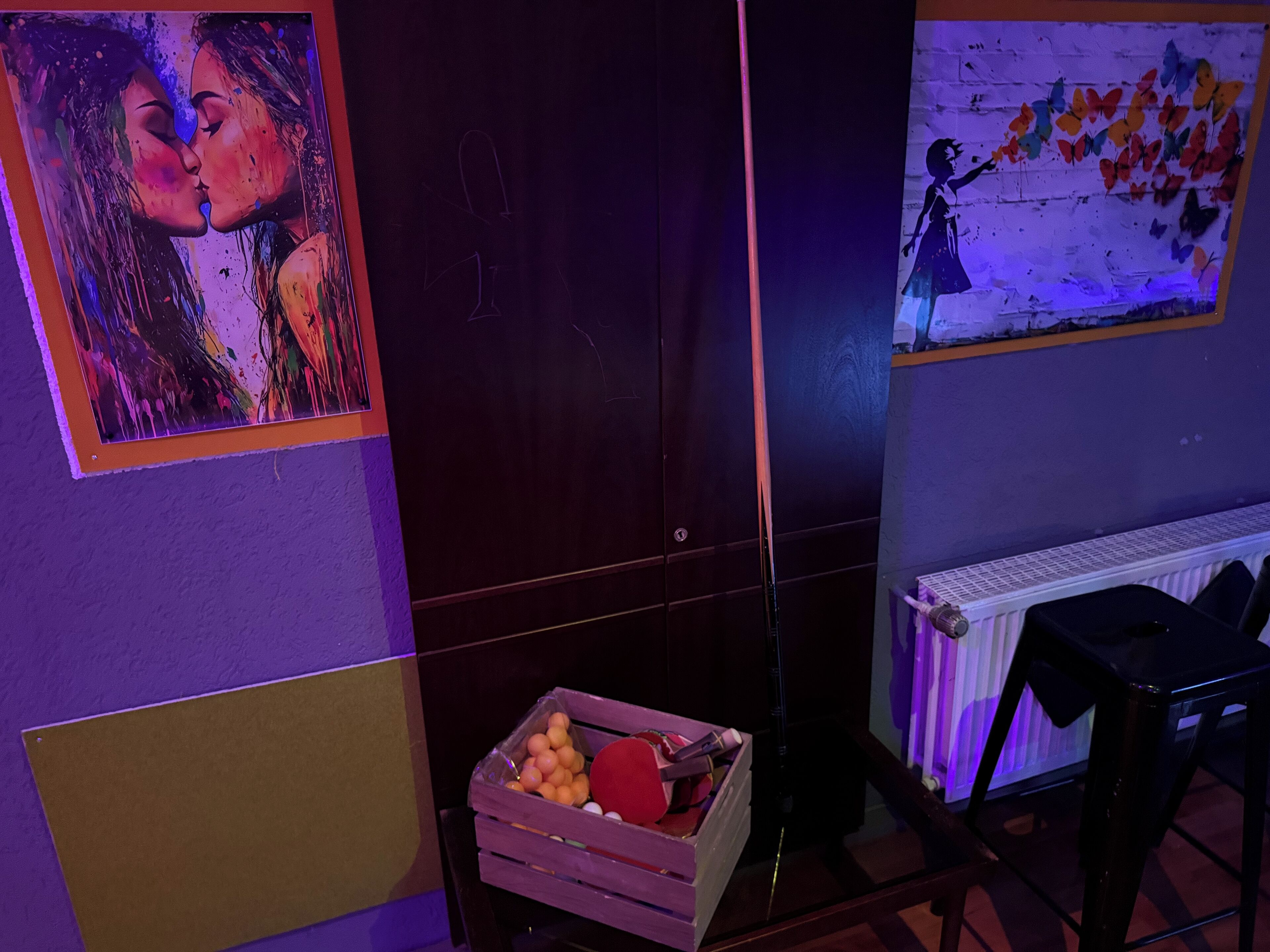 Une pièce avec une porte en bois, un radiateur, un mur orné d’une fresque représentant des papillons et une caisse remplie d’oranges.