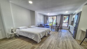 A modern hotel room with a large bed, a sofa, a dining table, and a kitchen area.