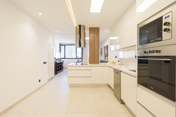 A modern kitchen with white cabinetry, a central island, and built-in appliances including a microwave and oven.