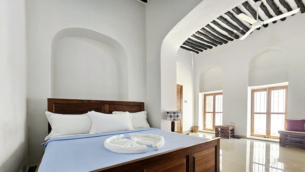 A spacious bedroom with a large bed, wooden headboard, and a blue bedspread. - Hello Rafiki House - Stonetown (Zanzibar Town)