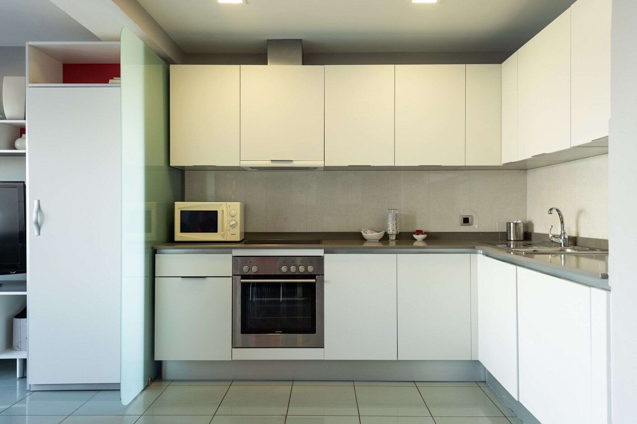 A modern kitchen with white cabinets, a microwave, an oven, and a sink.