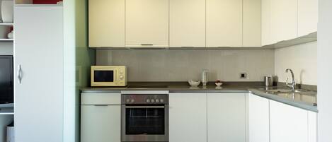 A modern kitchen with white cabinets, a microwave, an oven, and a sink.