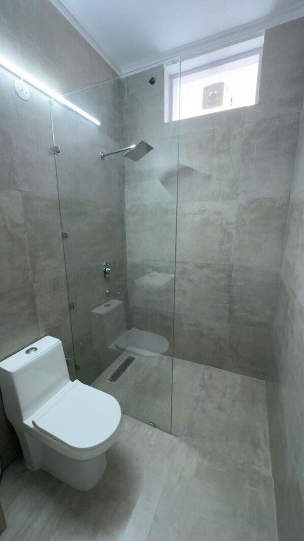 A bathroom with a glass-enclosed shower, a toilet, and a small window. - The Aana Hotel Sohna Gurgaon  (Sohna)