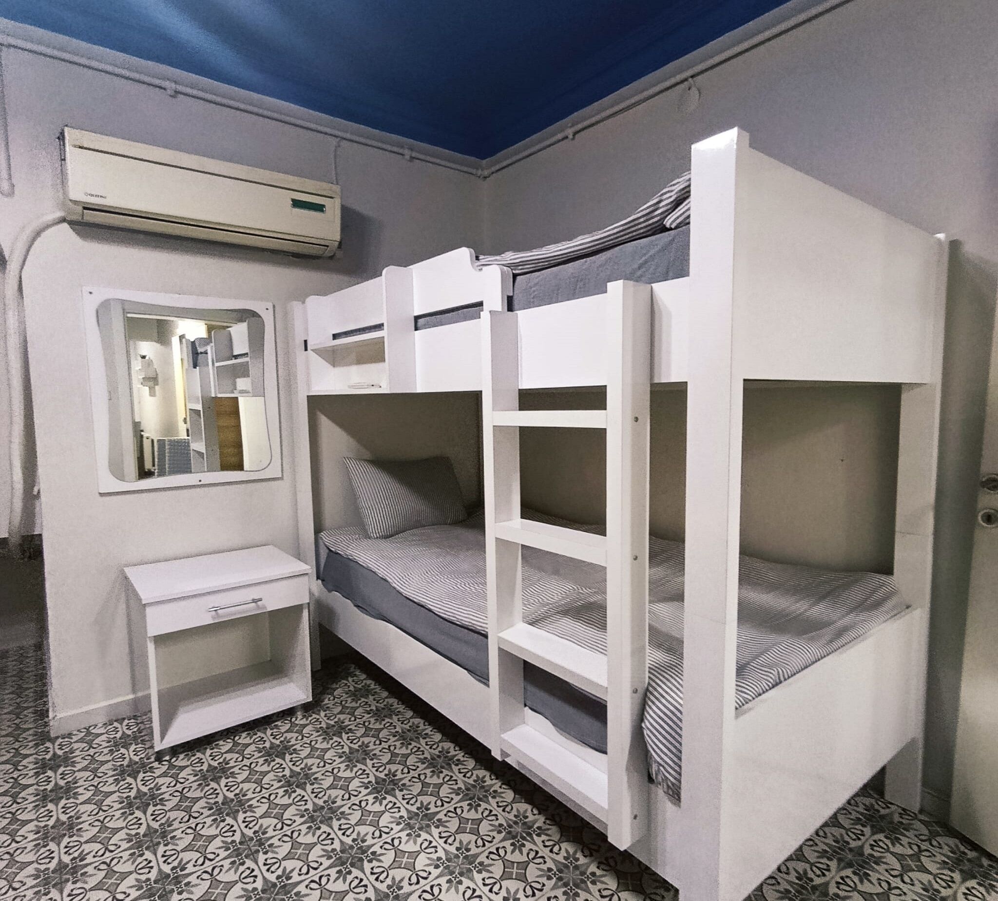 Quarto com beliche, uma escrivaninha pequena e um espelho.