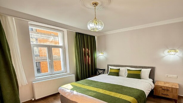 Ein Schlafzimmer mit Bett, einem Fenster mit Vorhängen, einem Heizkörper, einem Nachttisch aus Holz und einer Kristallleuchtre.