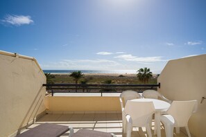 Un balcon donnant sur la plage, des chaises en plastique blanc et un sol carrelé.