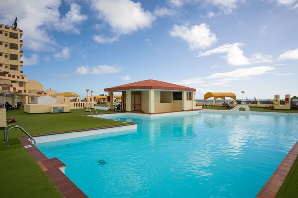 A swimming pool with a lifeguard tower, a covered seating area, and a view of the sea.