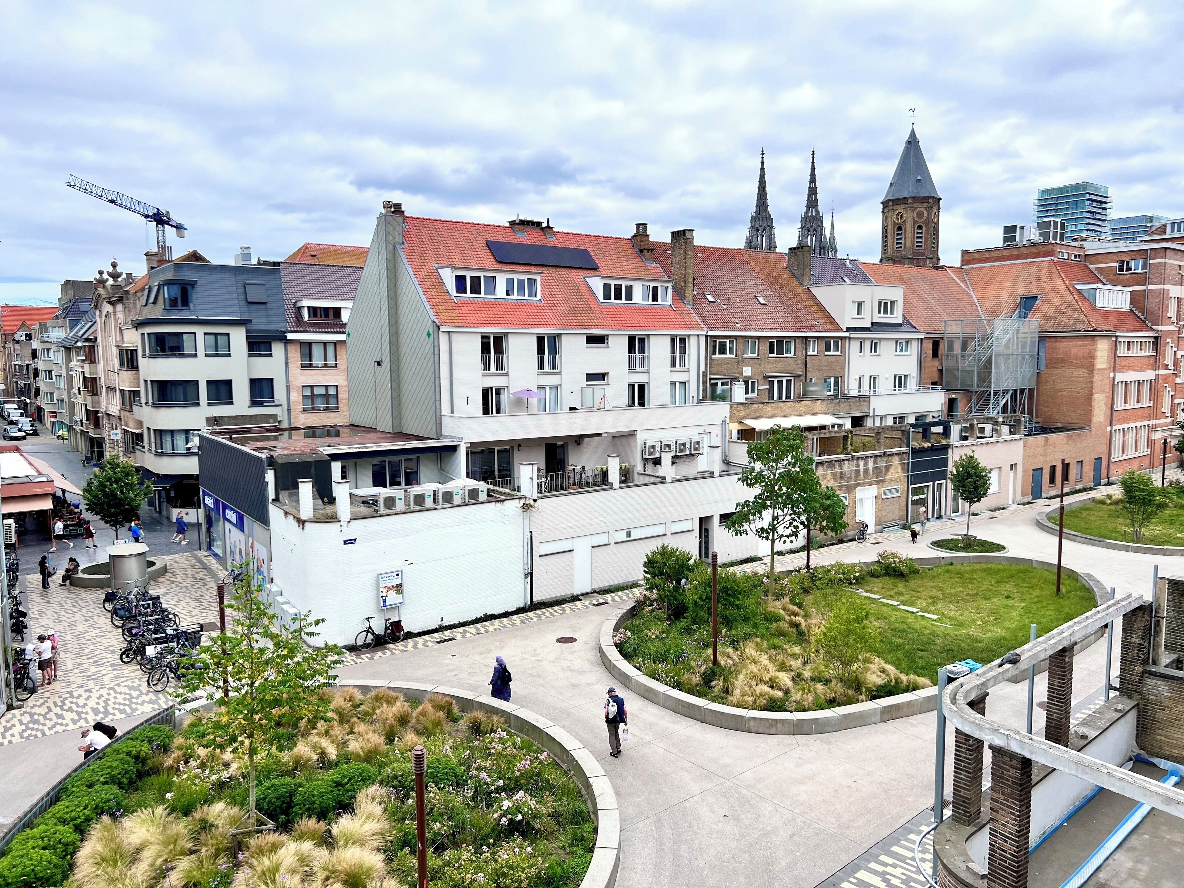 Stadsgezicht met historische gebouwen, een centraal plein met groen en een modern gebouw met een gebogen balkon.