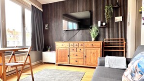 Ein Wohnzimmer mit einem Holzschrank, einem grauen Sofa, einem Holztisch mit Stühlen und einem großen Fenster.