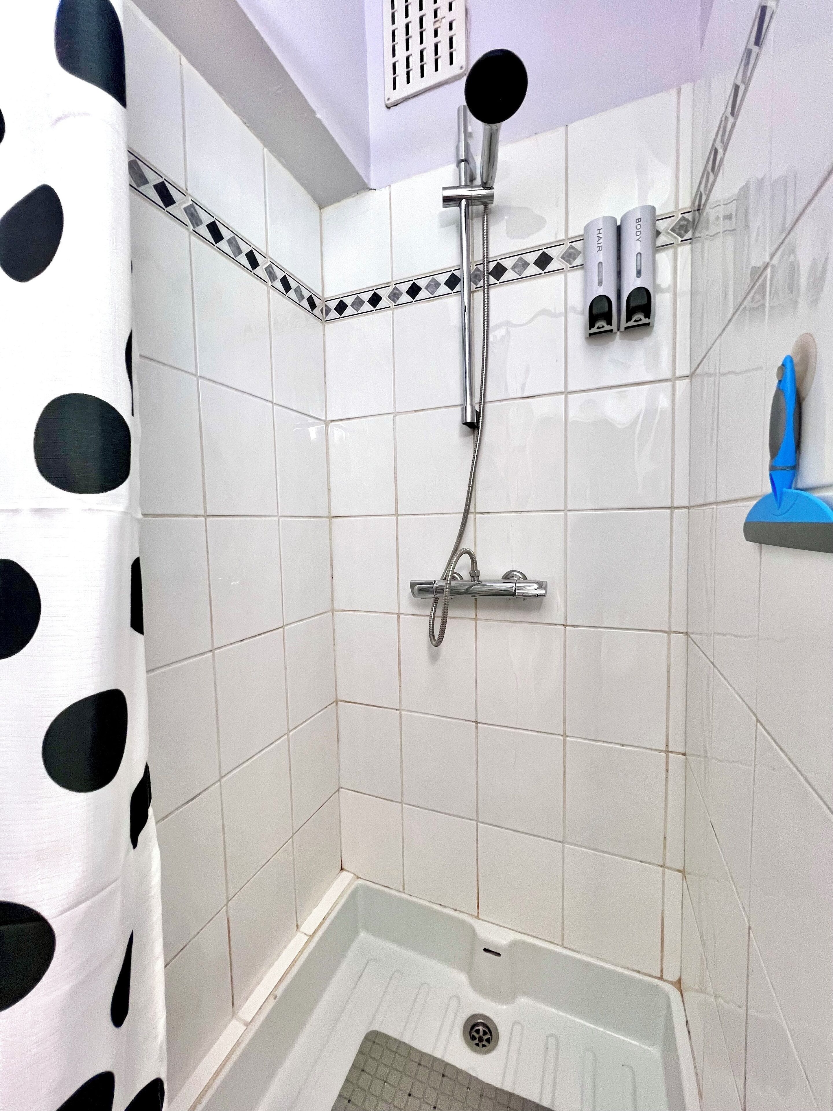 A shower with a handheld showerhead, a wall-mounted faucet, and a blue soap dispenser.