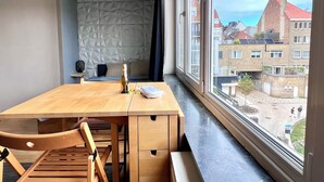 Ein Zimmer mit Holztisch und -stühlen, einer Weinflasche und Blick auf Gebäude durch große Fenster.
