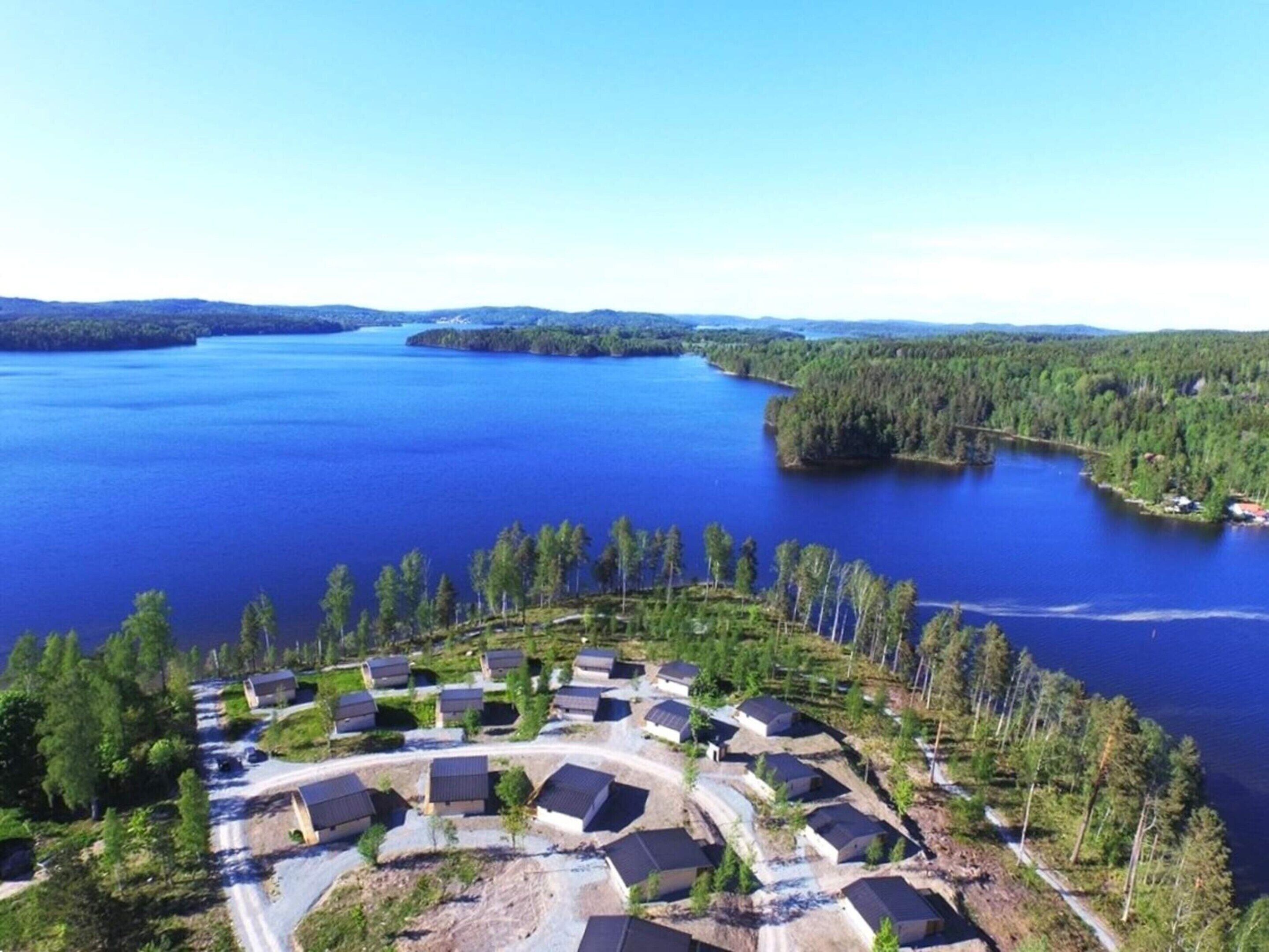 An aerial view of a lakeside resort with multiple buildings arranged in a semi-circular pattern, surrounded by dense forests and a large body of water.
