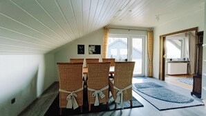 A dining area with a table and chairs, a view to the outside, and a window with curtains. - Apartment with panoramic balcony with reading material, games and fitness room (Gernsbach)