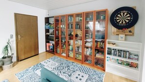 A room with a wooden bookshelf, a dartboard, and a patterned rug. - Apartment with panoramic balcony with reading material, games and fitness room (Gernsbach)