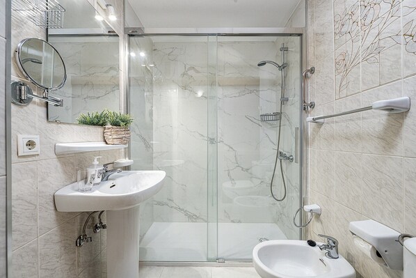 Un baño moderno con ducha envuelta en vidrio, lavamanos sobre pedestal y ducha de mano.