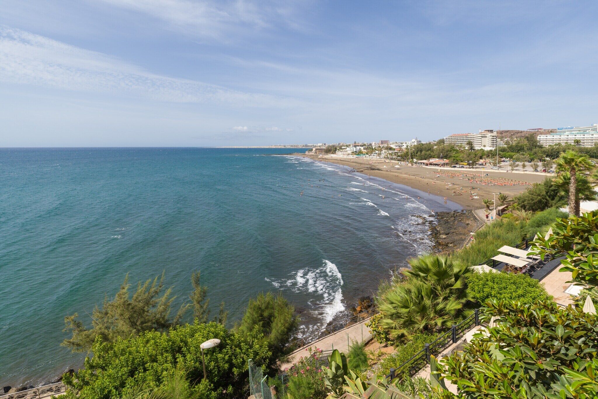 Vista costera con playa, océano y edificios al fondo.