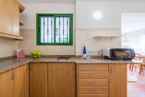 Una cocina con armarios de madera, un ventanal con marco verde, un tostador y un bol de fruta.