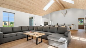 Un salon moderne avec un canapé d’angle, une table basse et un coin repas, la cuisine étant visible au fond.