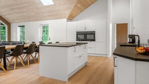 Une cuisine moderne avec des meubles blancs, un îlot central et un coin repas comprenant un canapé et des chaises.