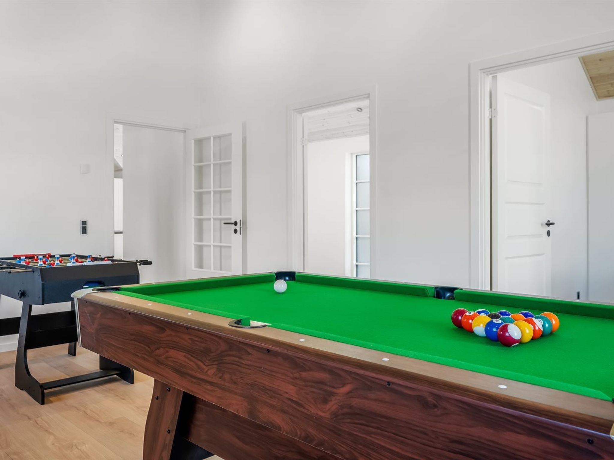 Uma mesa de bilhar com superfície de feltro verde, uma mesa de futebol de mesa e um conjunto de bolas de sinuca coloridas.
