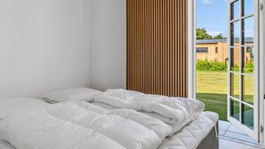 Une chambre avec un lit, un mur recouvert de lambris en bois et une grande porte vitrée donnant sur un espace extérieur.