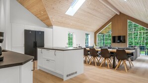 Une cuisine moderne avec des meubles blancs, un réfrigérateur noir et un plafond en bois agrémenté de lucarnes.