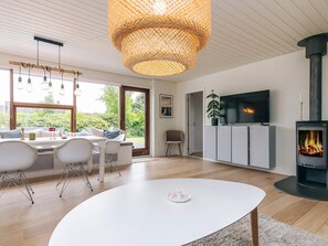 A modern living room with a white table, a TV mounted on a cabinet, and a wood-burning stove. - 4 Star Holiday Home in Albaek (Aalbaek)