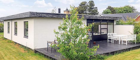 A modern house with a flat roof, a small deck, and a dining area with outdoor furniture.