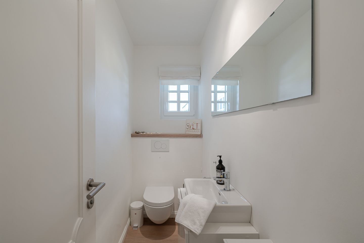 Un baño estrecho con inodoro, lavamanos y espejo.