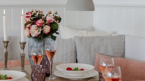 A dining table set with plates, glasses, and candles, with a vase of flowers and a pendant light above.