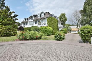 Une grande maison à deux étages, dotée d’un jardin aménagé et d’une allée pavée.