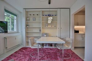 Une cuisine de taille réduite avec des meubles blancs, une table à manger et deux chaises, ainsi qu’un tapis rouge à motifs.