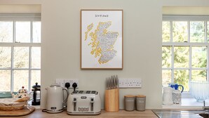 A kitchen with a framed Scotland map, a coffee maker, a kettle, a toaster, and a knife block. - Byre Cottage | Stravithie (Stravithie)