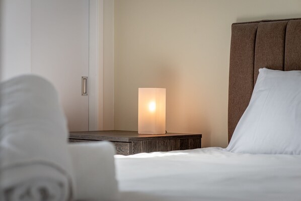 Ein ordentlich bezogenes Bett mit weißen Leinen, ein Nachttisch mit Lampe und ein braunes Kopfteil.