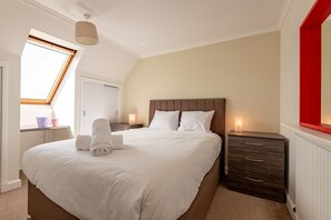 A bedroom with a large bed, a nightstand, a dresser, a skylight, and a red accent wall. - Kidston Court (No 9) (St Andrews)