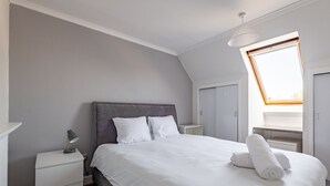 A neatly arranged bedroom with a large bed, a bedside lamp, a nightstand, and a window with a view. - Kidston Court (No 9) (St Andrews)