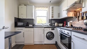 A compact kitchen with white cabinets, a washing machine, a microwave, and a stove. - Kidston Court (No 9) (St Andrews)