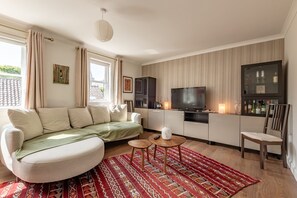 A modern living room with a sofa, a TV, a small table, and a patterned rug. - Kidston Court (No 9) (St Andrews)