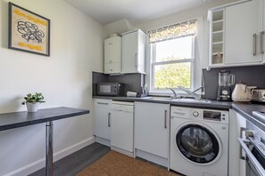 A compact kitchen with a dishwasher, microwave, sink, and washing machine. - Kidston Court (No 9) (St Andrews)
