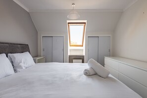 A bedroom with a large bed, two wardrobes, a skylight, and a small table. - Kidston Court (No 9) (St Andrews)