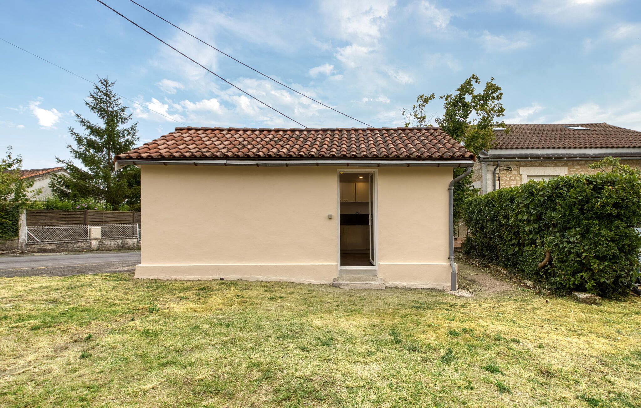 A small, single-story building with a tiled roof, a door leading to an interior space, and a grassy lawn in front.