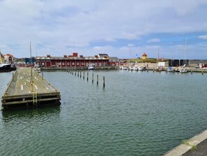 Un muelle de madera se adentra en aguas tranquilas, con una hilera de edificios rojos al fondo.
