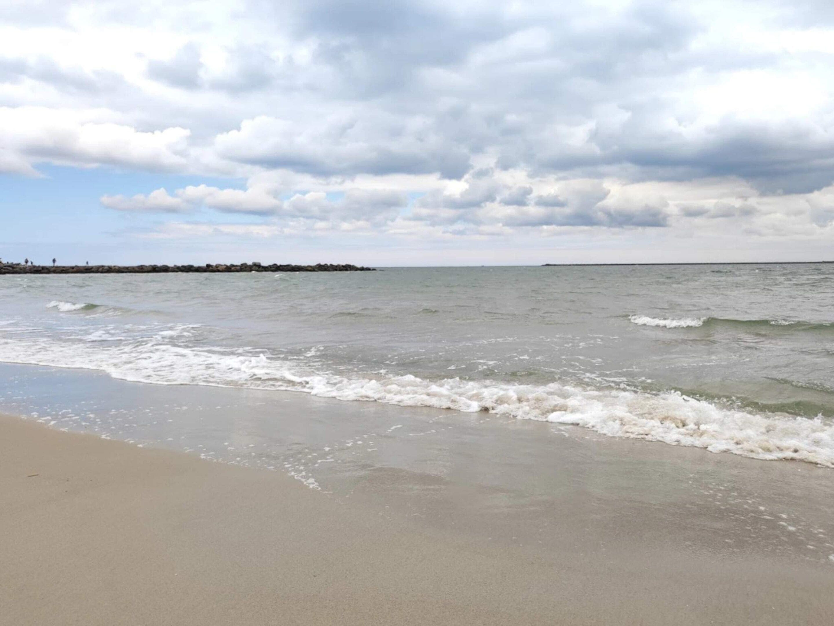 A beach with waves, a cloudy sky, and a distant shoreline.