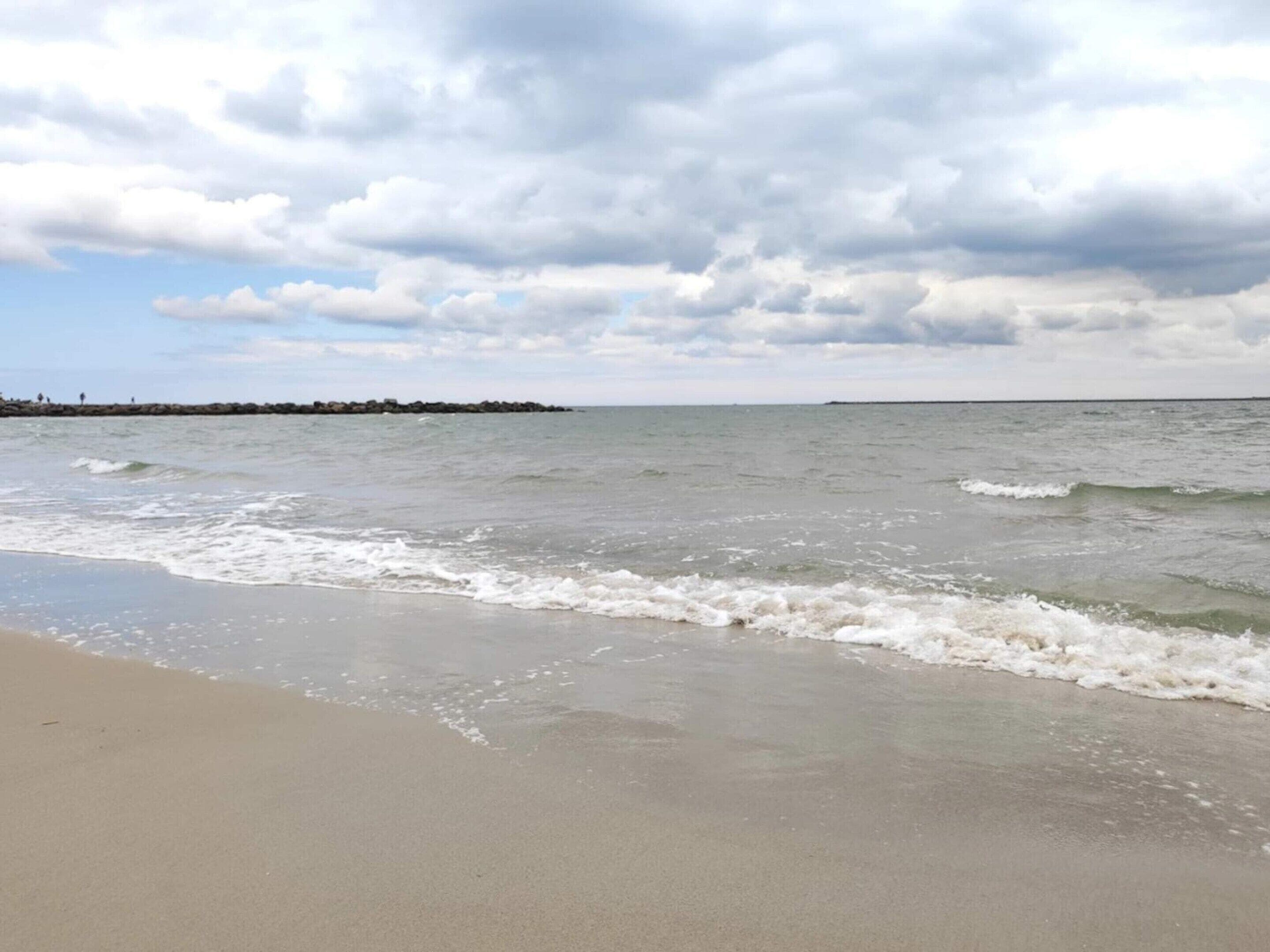 A beach with waves, a cloudy sky, and a distant shoreline.