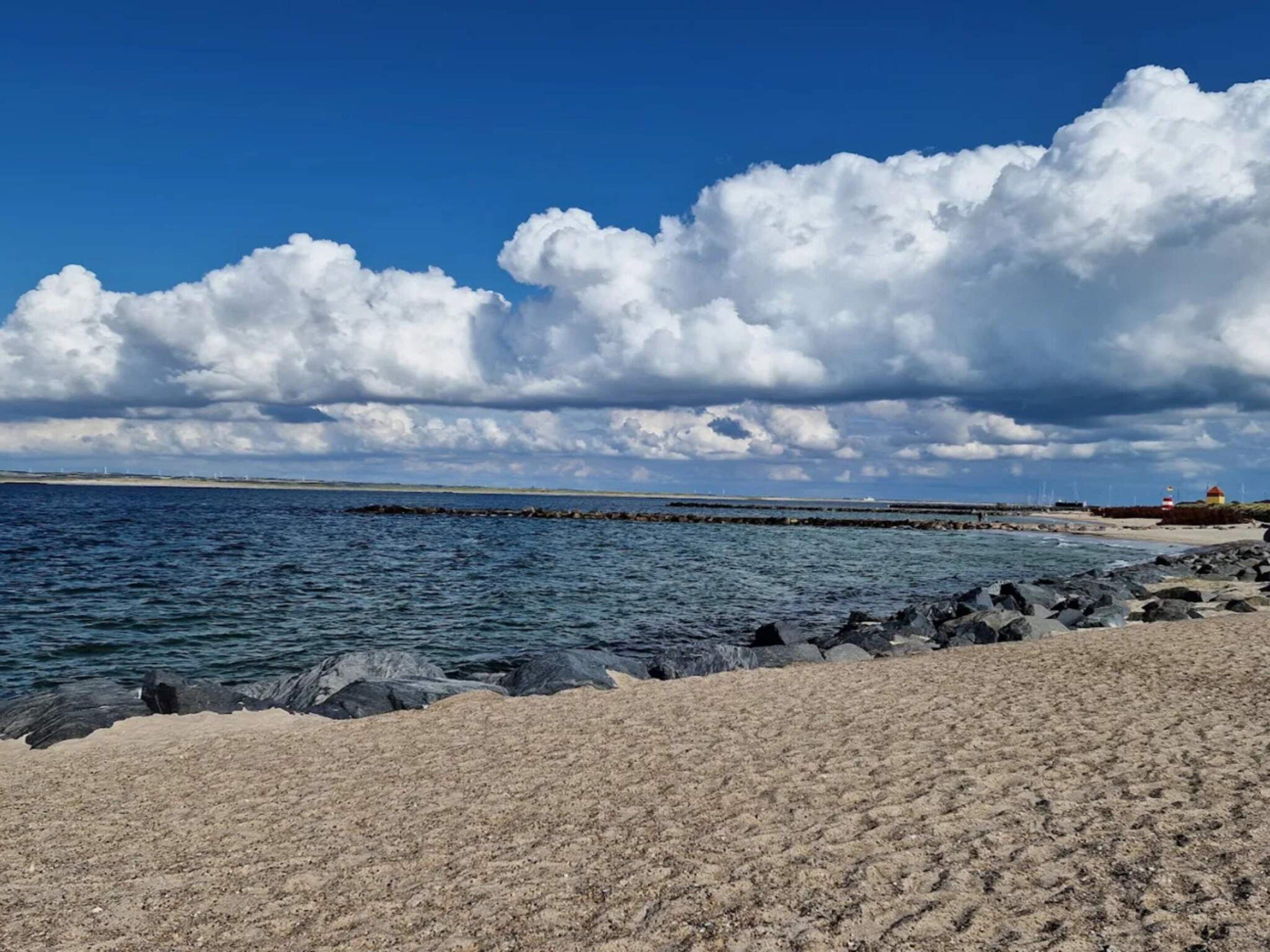 A coastal landscape with a sandy beach, rocky shoreline, and a lighthouse in the distance.