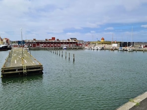 Un muelle de madera que se adentra en aguas tranquilas, con una hilera de edificios rojos al fondo.