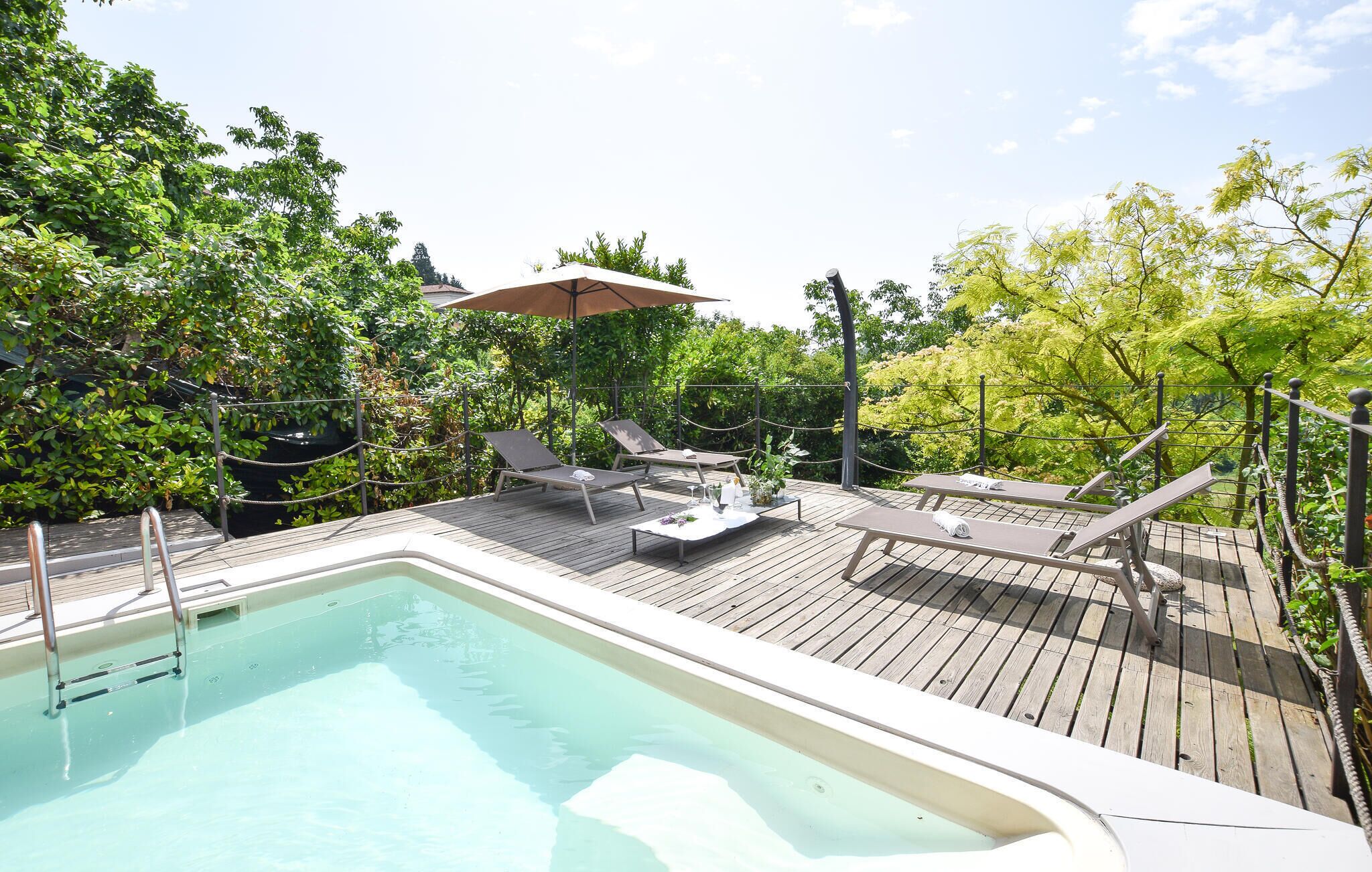 A wooden deck with a swimming pool, lounge chairs, and an umbrella.