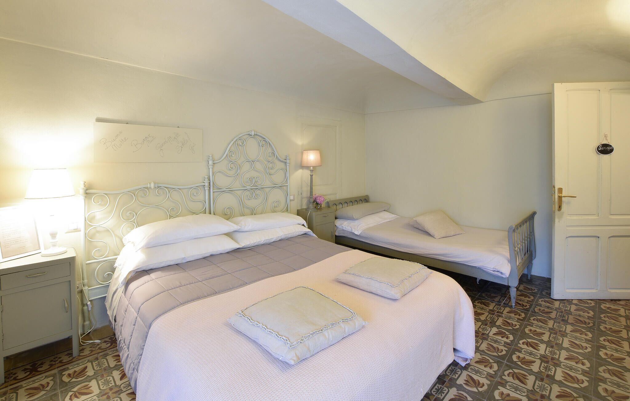 A bedroom with two beds, a nightstand with a lamp, a wall with a sign, and a door with a sign.